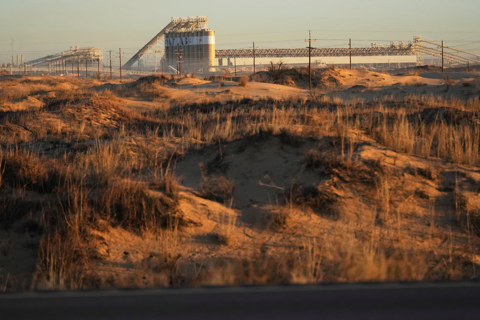 A sand dune is backdropped by Atlas Energy plant at the beginning of a 42-mile conveyor belt that carries sand needed for hydraulic fracturing Wednesday, Feb. 26, 2025, in Kermit, Texas. (AP Photo/Julio Cortez)