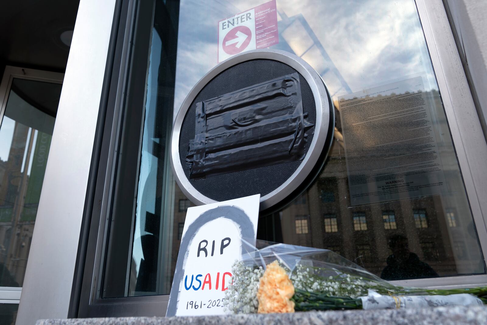 FILE - Flowers and a sign are placed outside the headquarters of the U.S. Agency for International Development, or USAID, Feb. 7, 2025, in Washington. (AP Photo/Jose Luis Magana, file)