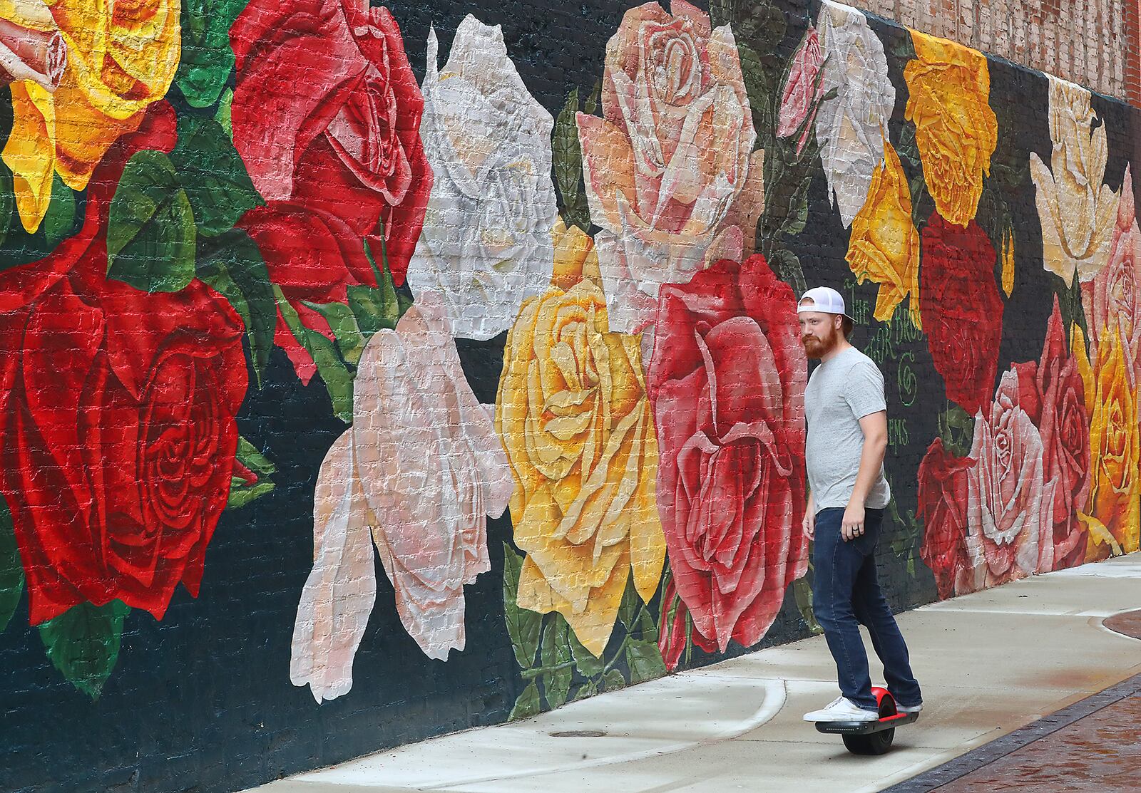 Aaron Jernigan rides his One Wheel electric skateboard in the  front of the Rose City mural along Main Street in Springfield. BILL LACKEY/STAFF