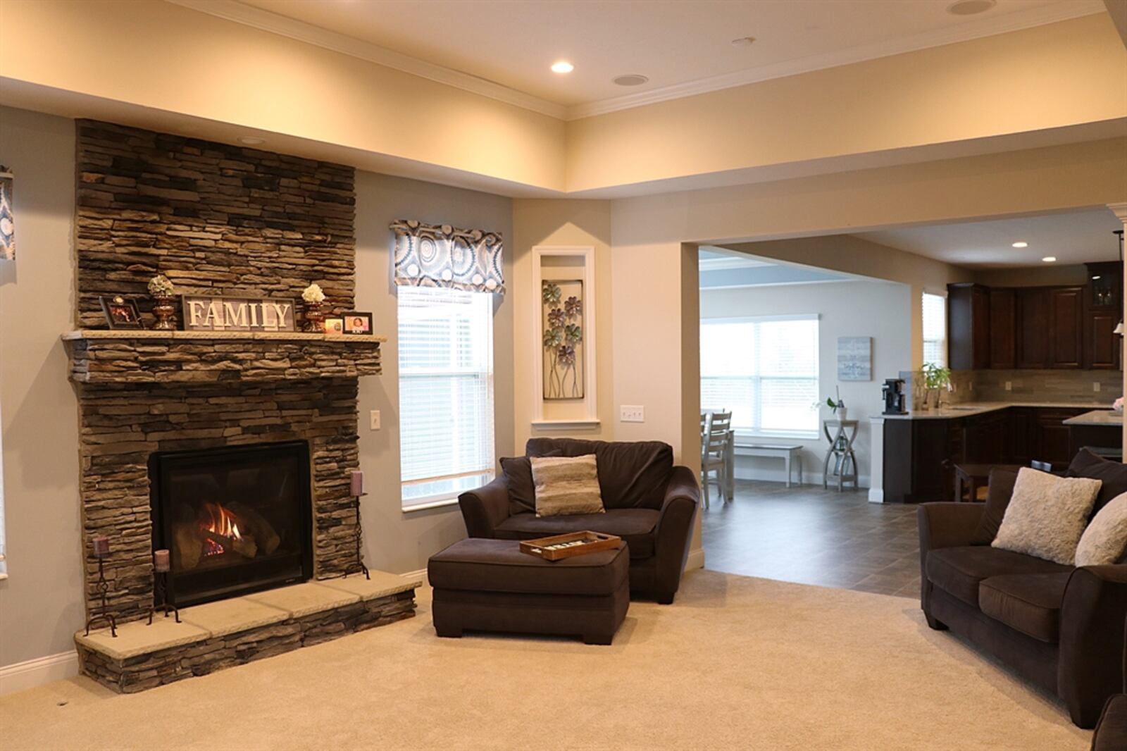 In the great room, a stack-stone gas fireplace with a stone hearth and mantel is flanked by two windows. 