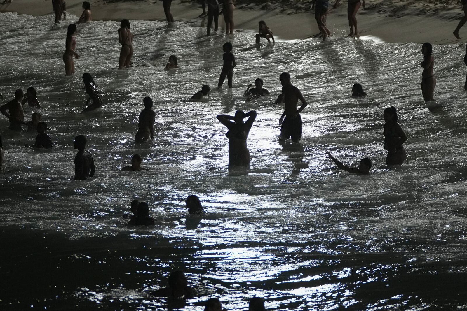 FILE - People wade in the waters of Arpoador beach as the sun sets in Rio de Janeiro, Jan. 23, 2025. (AP Photo/Silvia Izquierdo, File)