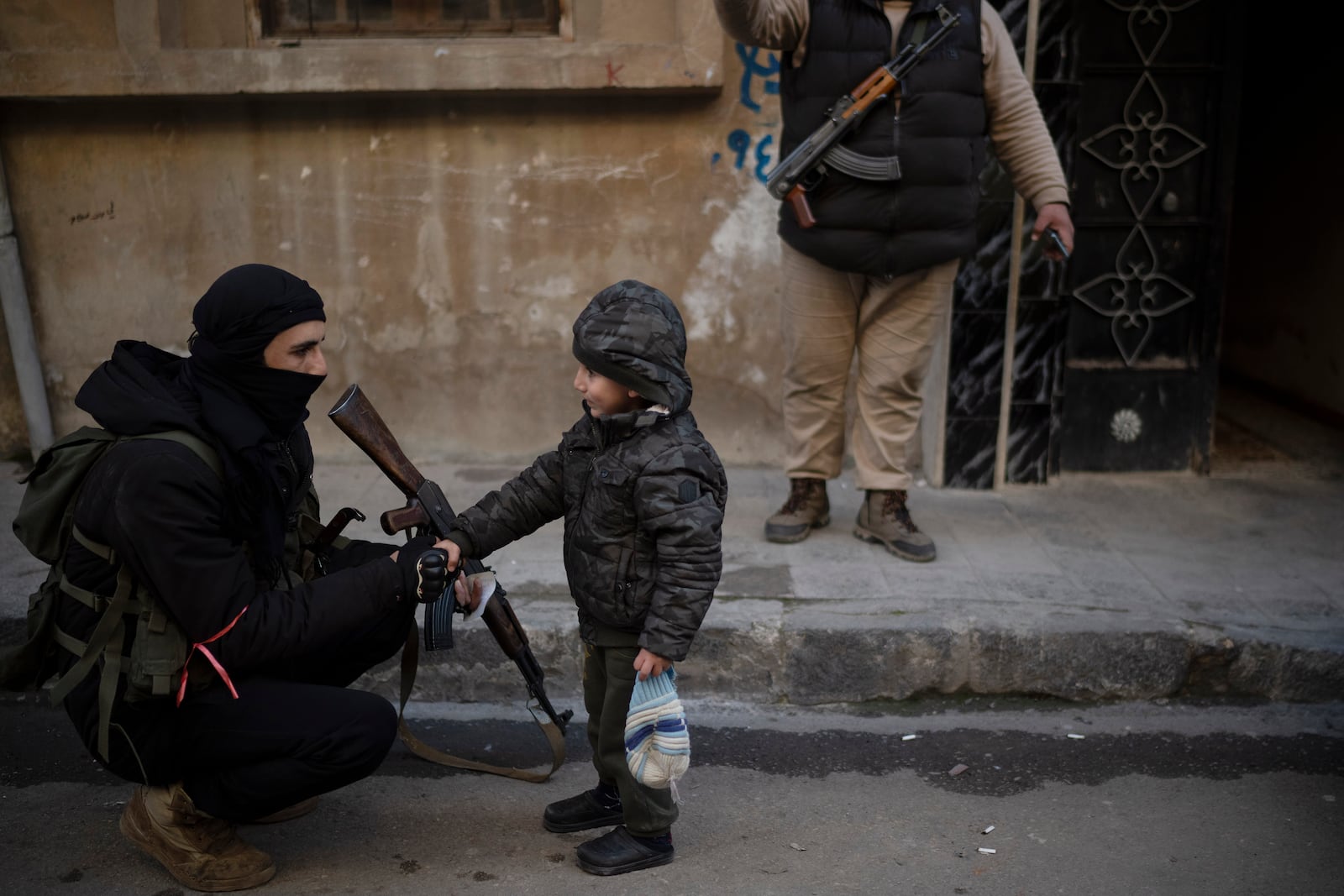 A member of the new security forces shakes hands with a boy during an operation to detain men suspected of being part of militias or loyalist soldiers of the ousted president Bashar Assad in Homs, Syria, Friday, Jan. 3, 2025. (AP Photo/Leo Correa)