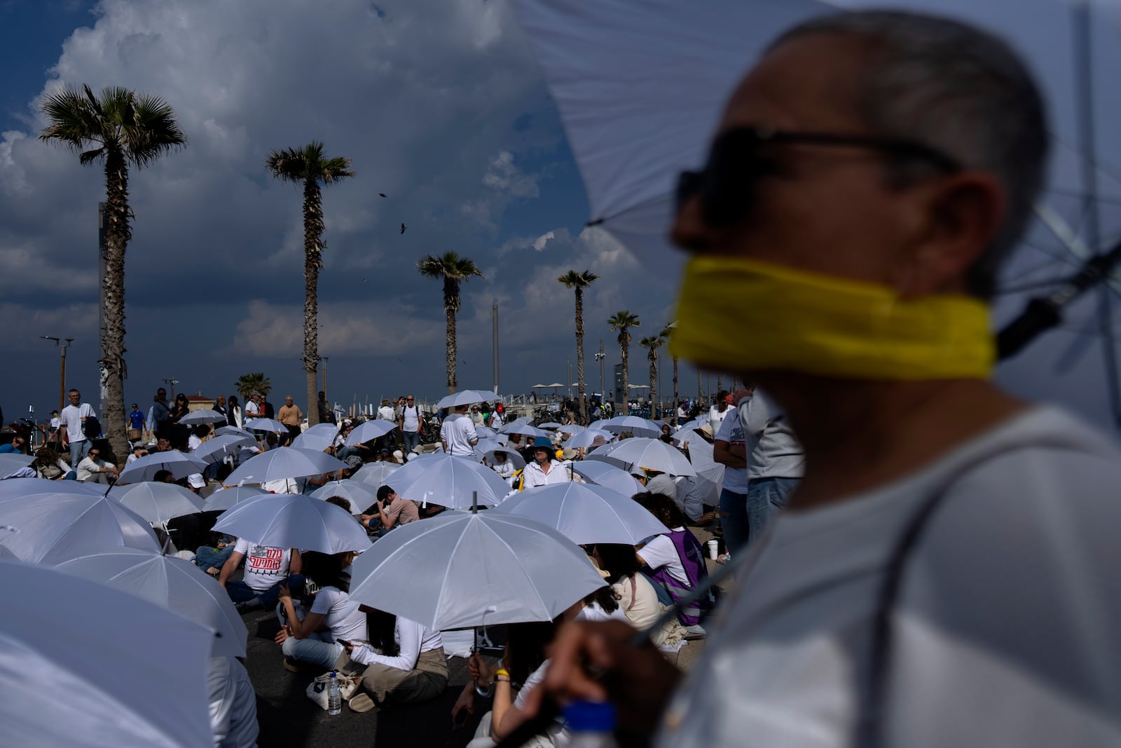 Activists sit on a road with white umbrellas during a protest calling for the release of hostages held in the Gaza Strip, in front of the U.S. Embassy branch office in Tel Aviv, Israel, Friday, Jan. 31, 2025. (AP Photo/Oded Balilty)