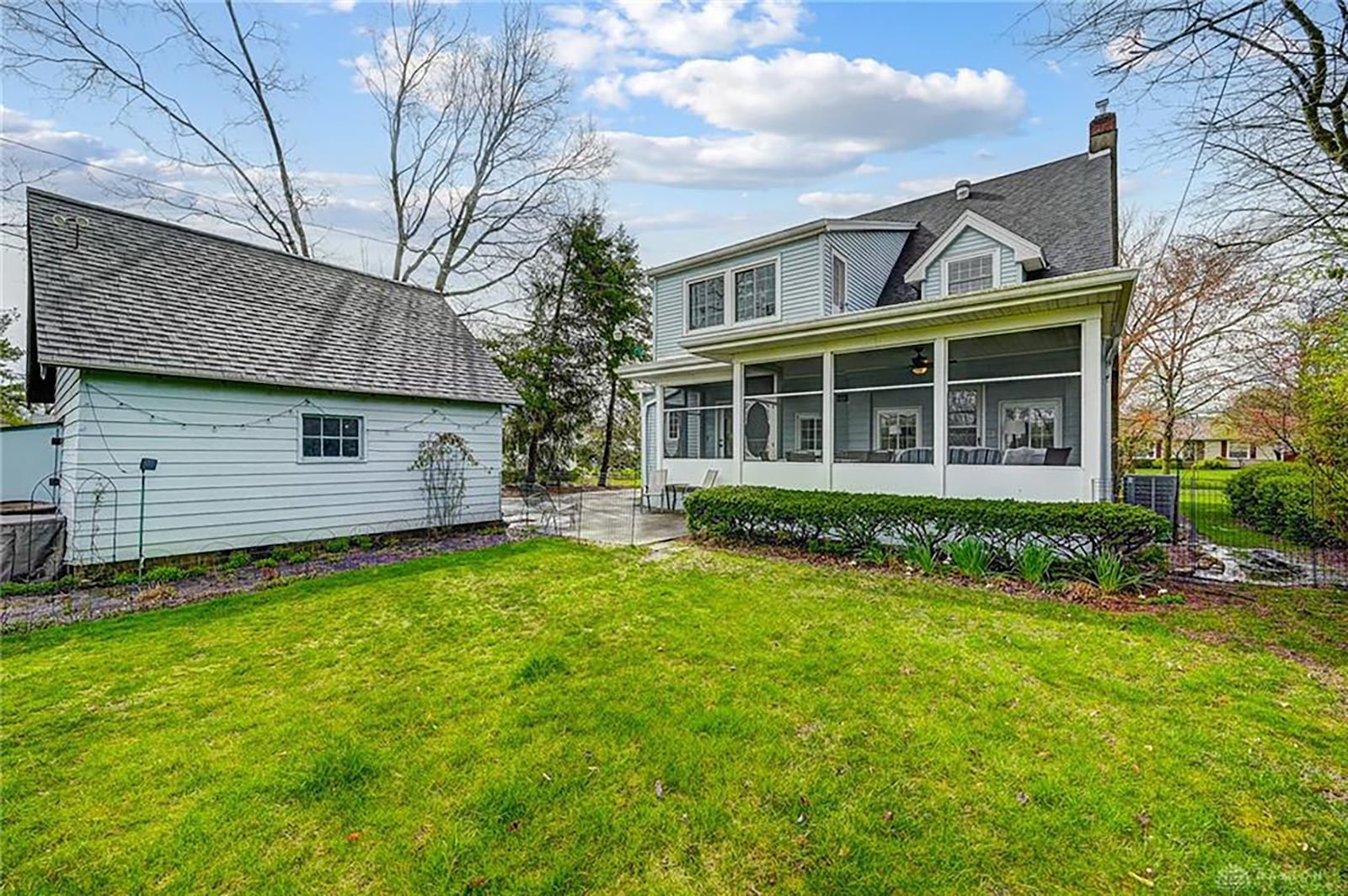 The rear of the home has a screen and glass sun porch, a concrete patio, a shed attached to the garage and heavy landscaping. The yard is partially fenced.