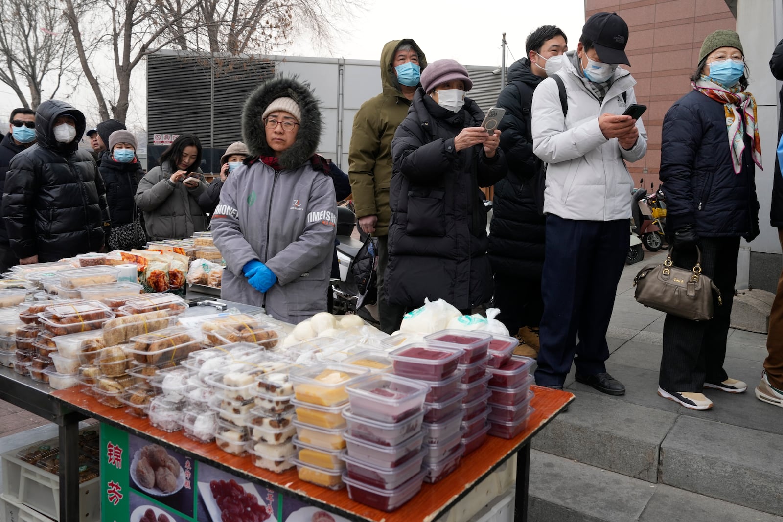 Residents line up near a table of assorted snacks to buy yuanxiao, a traditional Chinese food made with glutinous rice flour and sweet fillings consumed as part of the upcoming Lantern Festival celebrations, at the Jinfang Snacks Shop in Beijing, Tuesday, Feb. 11, 2025. (AP Photo/Ng Han Guan)