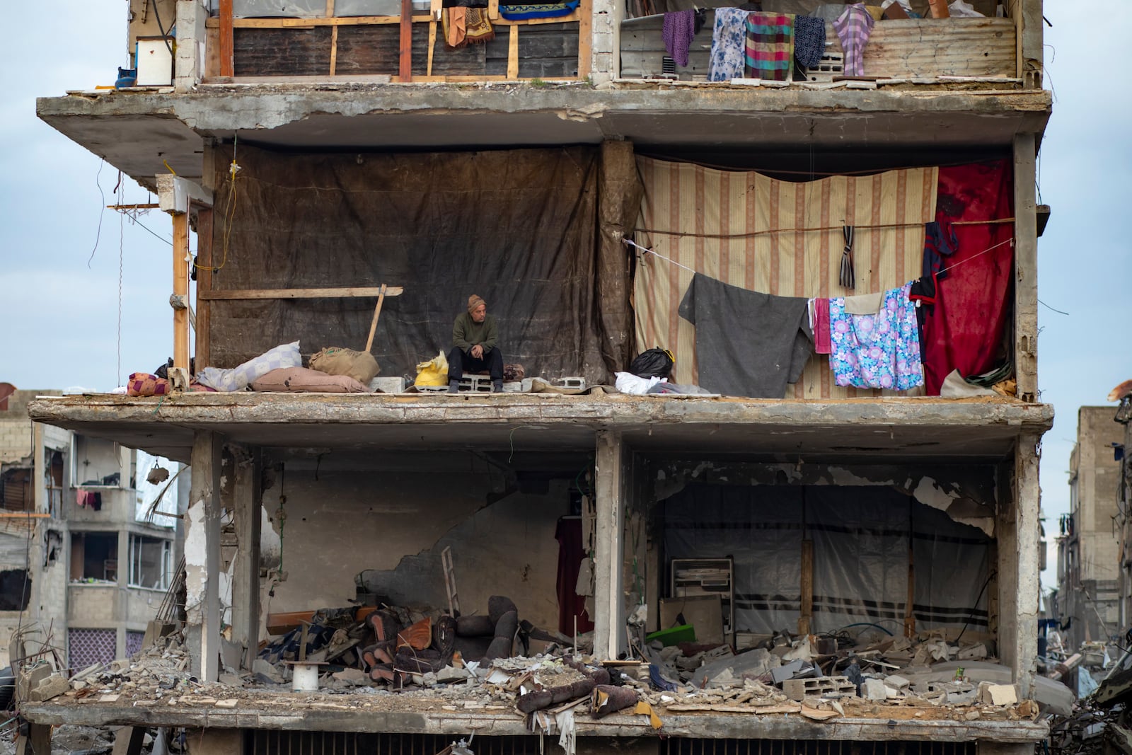 A man sits in his partially standing home, covered with sheets as makeshift walls, in an area largely destroyed by the Israeli army's air and ground offensive in Jabaliya, Gaza Strip, on Tuesday, Feb. 11, 2025. (AP Photo/Jehad Alshrafi)