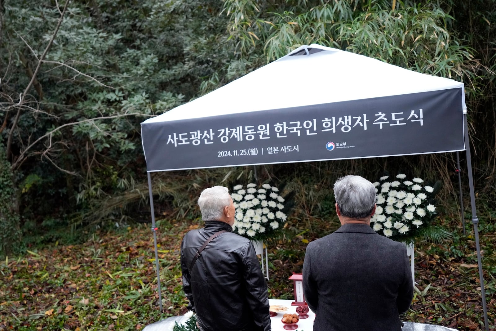 Relatives of Korean victims and South Korean officials offer a prayer during a memorial service at the site of former Fourth Souai Dormitory for the mine workers from the Korean Peninsula, in Sado, Niigata prefecture, Japan, Monday, Nov. 25, 2024, a day after boycotting a memorial organized by Japanese officials. The black banner reads "A memorial service for Korean forced laborer victims at Sado Mine." (AP Photo/Eugene Hoshiko)