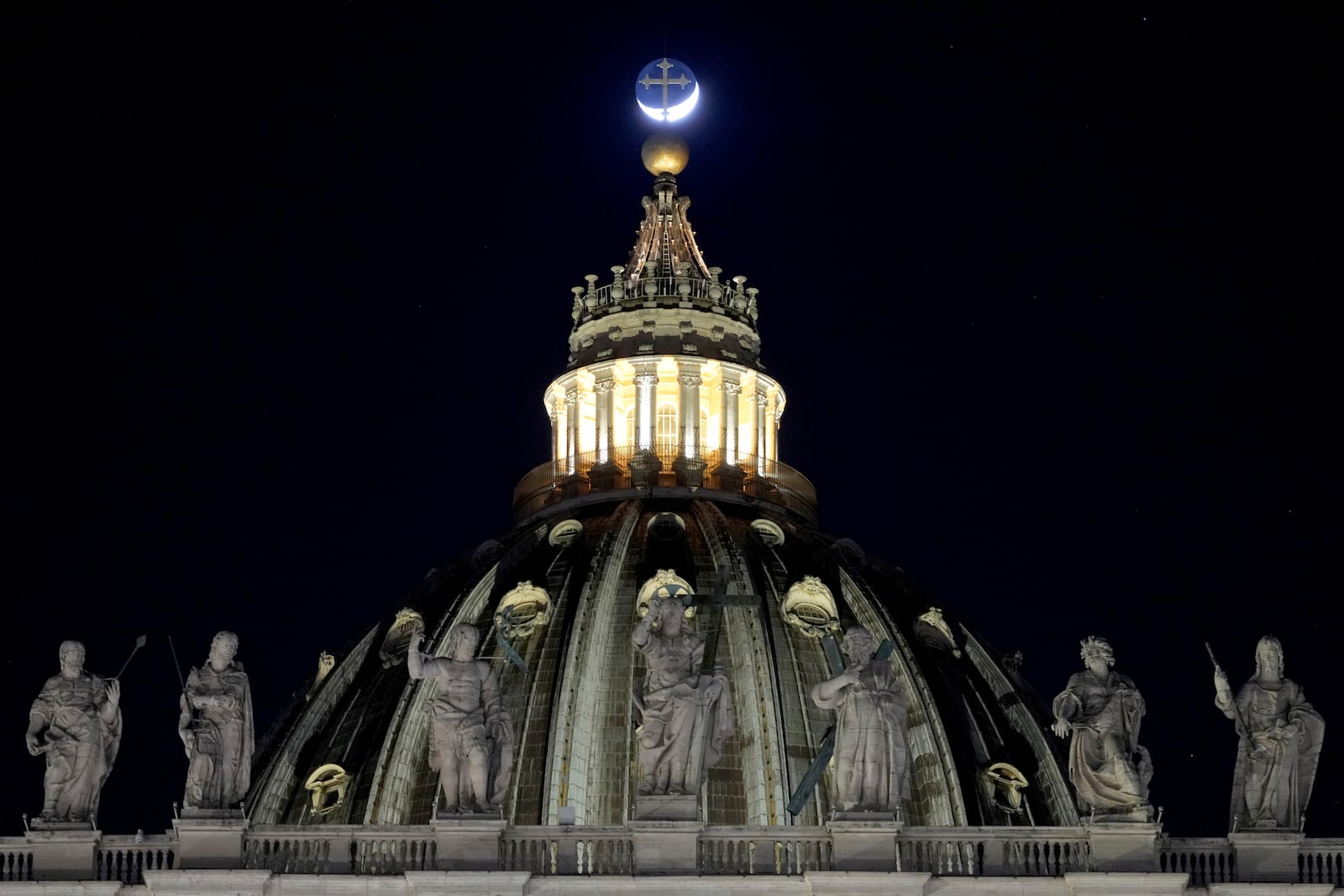 The moon moves behind the cross on top of St Peter's Basilica ahead of the recitation of the Holy Rosary for Pope Francis' health in St Peter's Square at the Vatican, Monday, March 3, 2025. (AP Photo/Kirsty Wigglesworth)