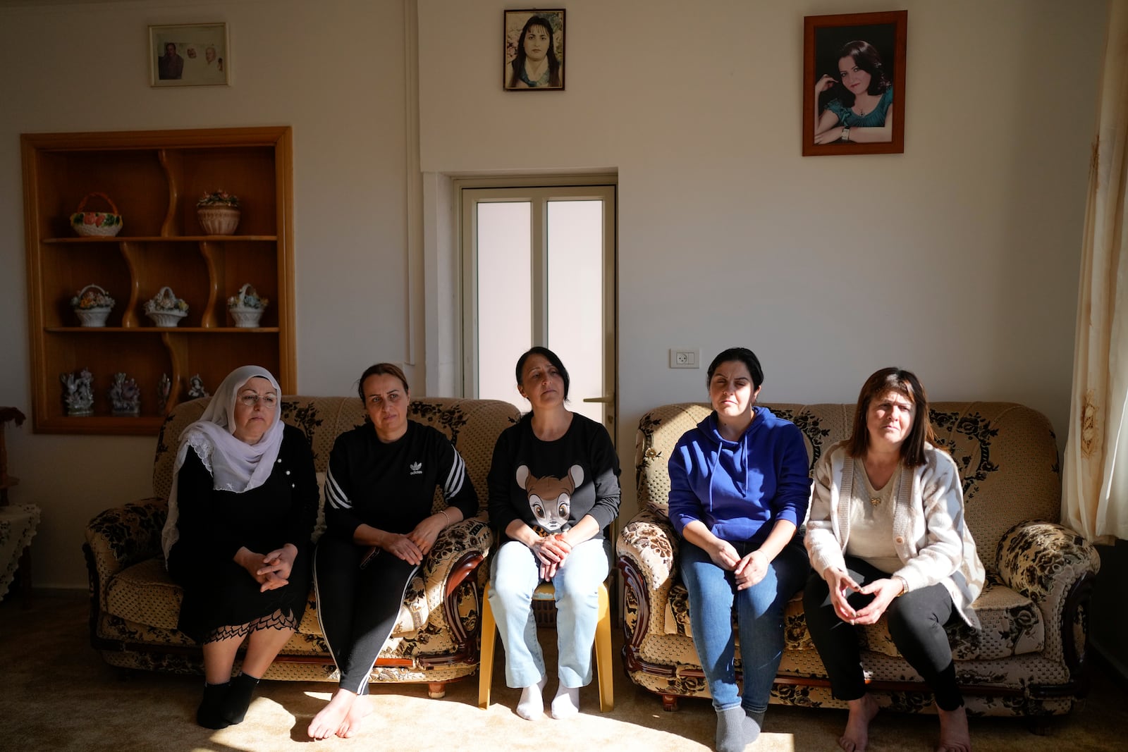 Five of six Safadi sisters sit on a couch under a portrait of their sister, Sawsan, who lives inside the buffer zone near the "Alpha Line" that separates the Israeli-controlled Golan Heights from Syria, in the town of Majdal Shams, Wednesday, Dec. 18, 2024. (AP Photo/Matias Delacroix)