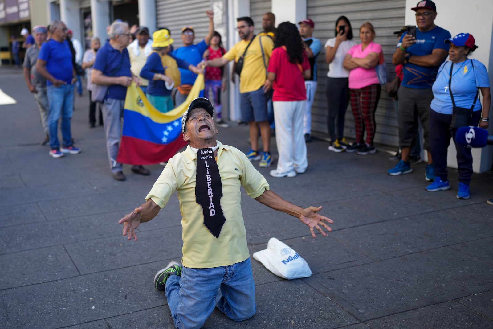 A man wearing the phrase in Spanish "Fight for freedom" kneels during a demonstration by opponents of Venezuelan President Nicolas Maduro the day before his inauguration for a third term in Caracas, Venezuela, Thursday, Jan. 9, 2025. (AP Photo/Matias Delacroix)