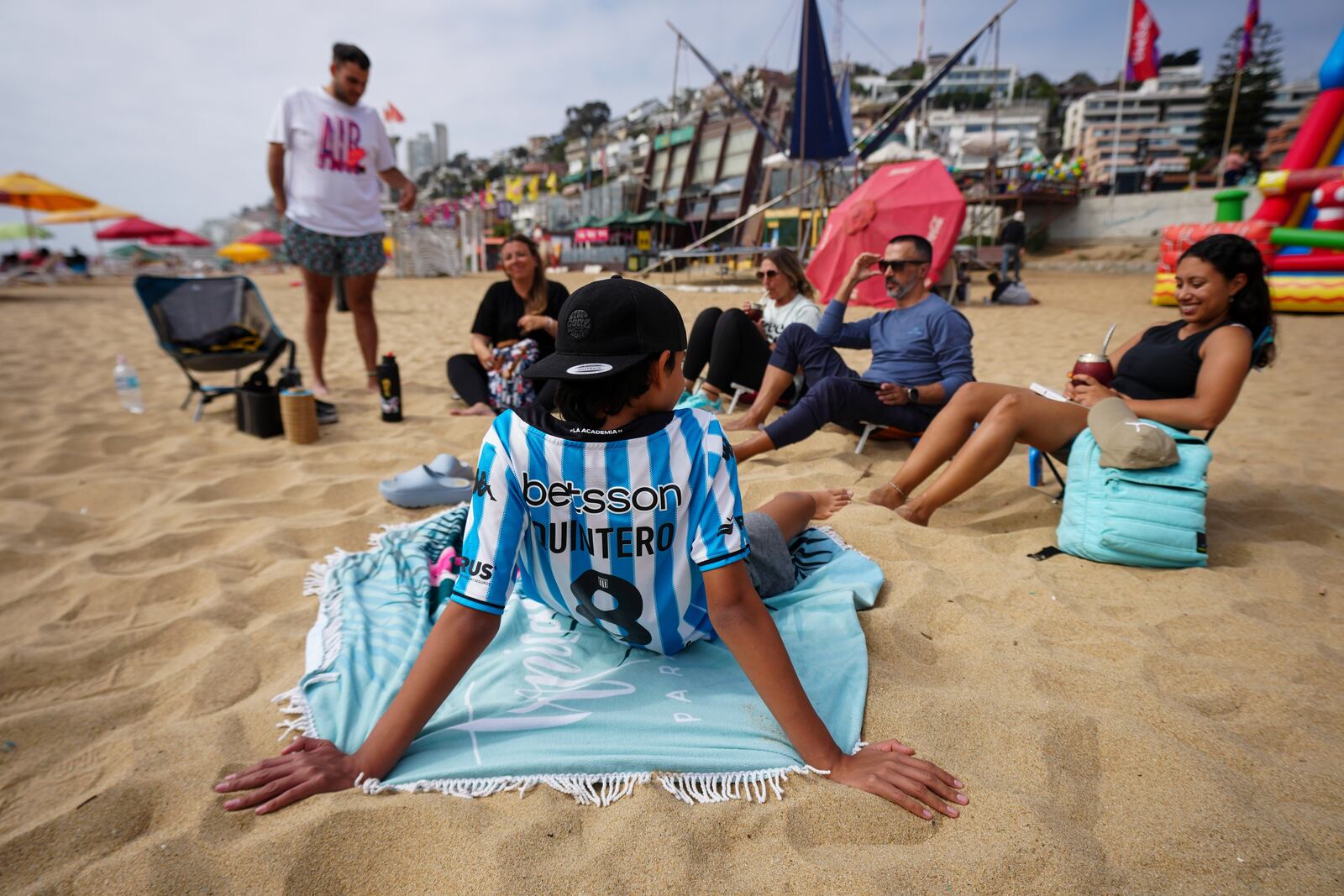 Argentine Cristian Vázquez, adjusting his sunglasses in the background, lounges on the sand with friends and family at Renaca beach in Vina del Mar, Chile, Thursday, Jan. 30, 2025. (AP Photo/Esteban Felix)