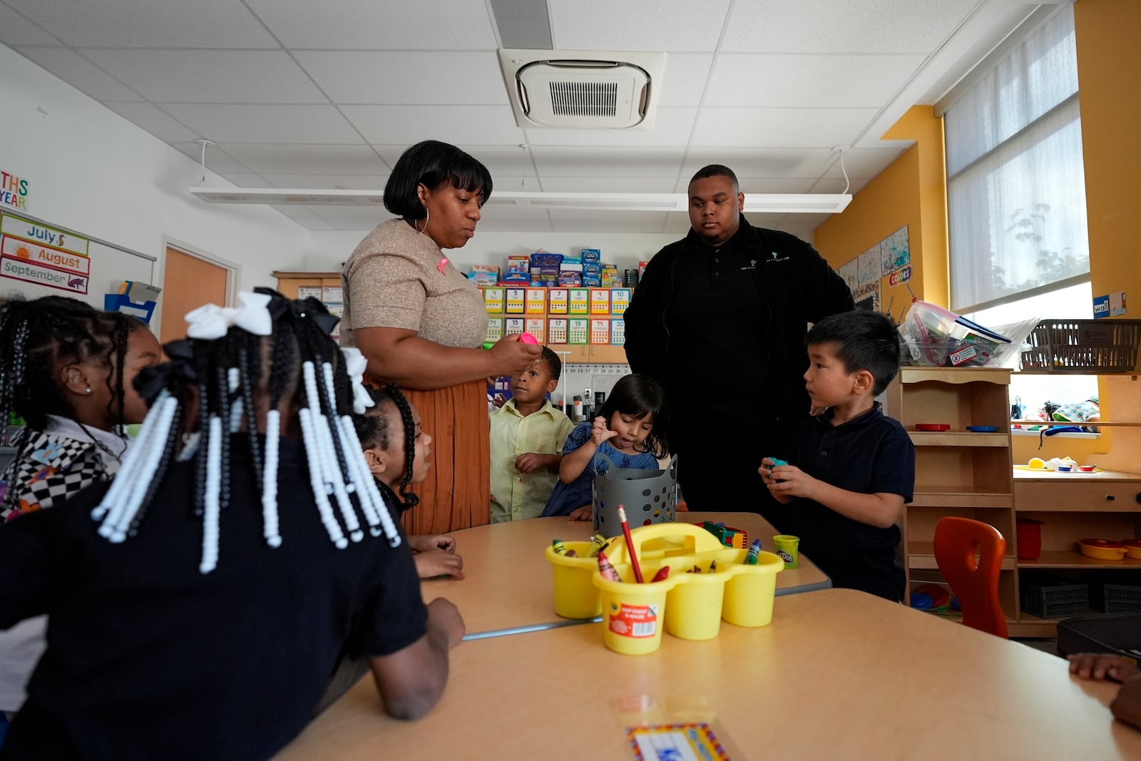 Preschool teacher Bridget Jeffreys and Leading Men fellow Davontez Johnson are surrounded by students while distributing playdough for an activity, Thursday, Oct. 3, 2024, at Dorothy I. Height Elementary School in Baltimore. (AP Photo/Stephanie Scarbrough)