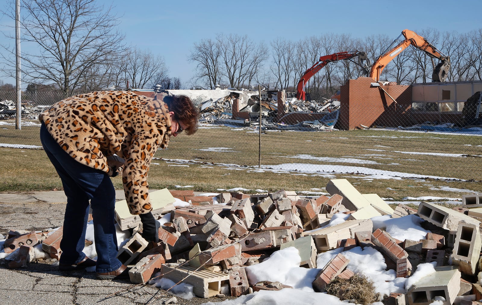 Kim Bachman looks through a pile of bricks from Northridge Elementary/Middle School as a wrecking crew demolishes the building Monday, Feb. 19, 2024. The school has been empty since the students moved into a combined Kenton Ridge School at the beginning of the school year. BILL LACKEY/STAFF