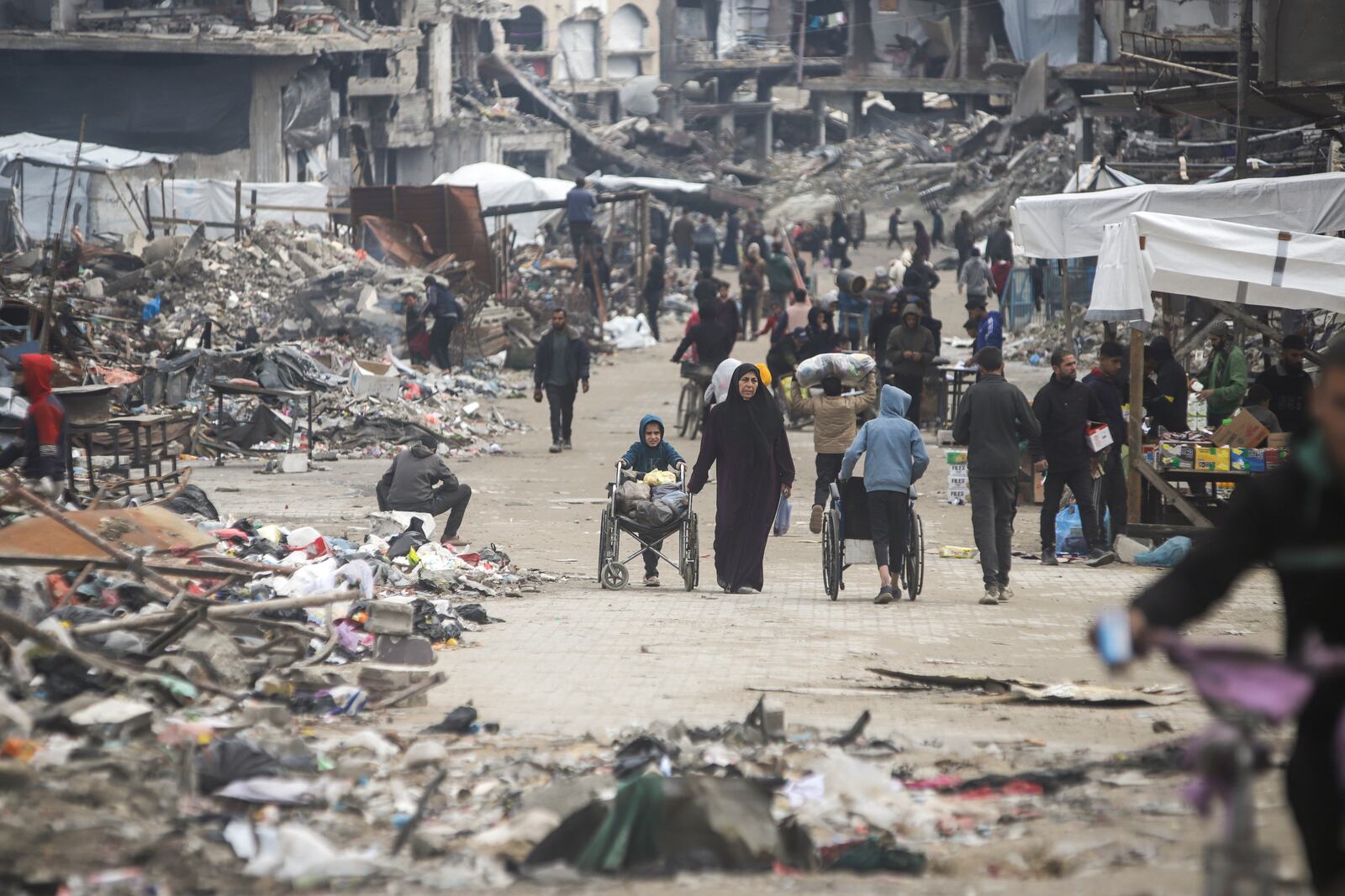 Pedestrians walk along a road lined with few stands selling goods, amid widespread destruction caused by the Israeli military's ground and air offensive in Gaza City's Jabaliya refugee camp, Friday, Feb. 7, 2025. (AP Photo/Jehad Alshrafi)