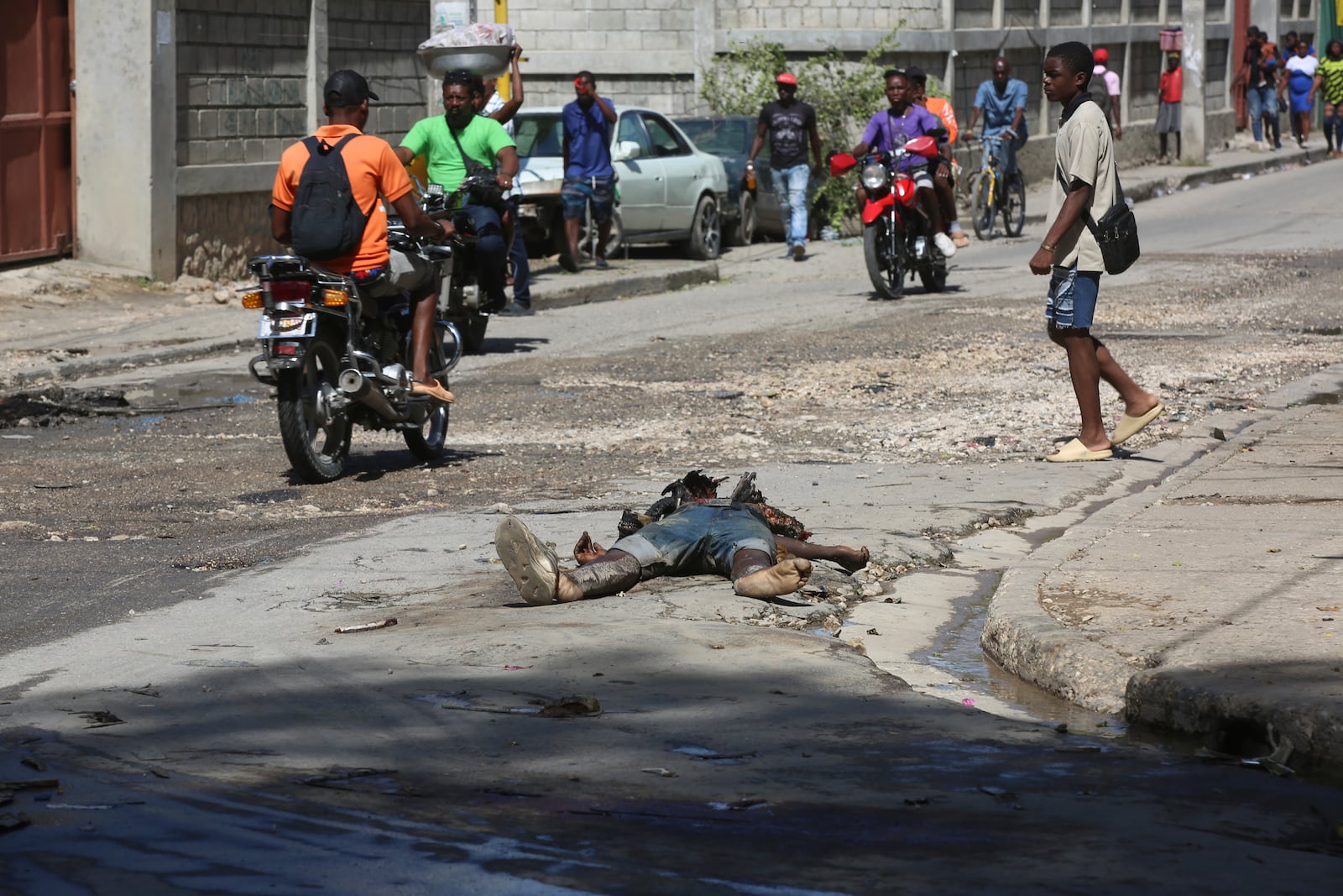 Pedestrians walk past the decomposing body of a man left abandoned on a street in downtown Port-au-Prince, Haiti, Wednesday, Nov. 13, 2024. (AP Photo/Odelyn Joseph)