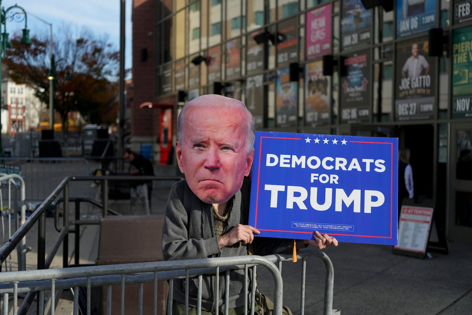 A Donald Trump supporter wearing a cutout face of President Joe Biden holds a sign outside a Trump rally in Reading, Pa., Monday, Nov. 4, 2024. (AP Photo/Luis Andres Henao)