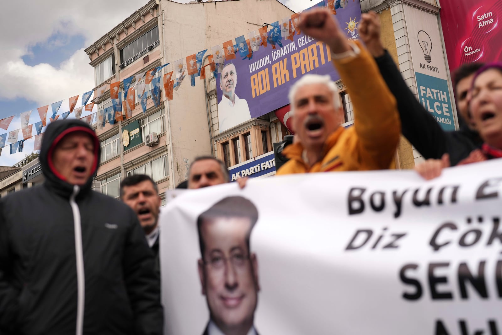 Backdropped by a billboard featuring a photo of Turkey's President Recep Tayyip Erdogan, people chant slogans as they protest outside the Vatan Security Department, where Istanbul Mayor Ekrem Imamoglu is expected to be taken following his arrest in Istanbul, Turkey, Wednesday, March 19, 2025. (AP Photo/Francisco Seco)