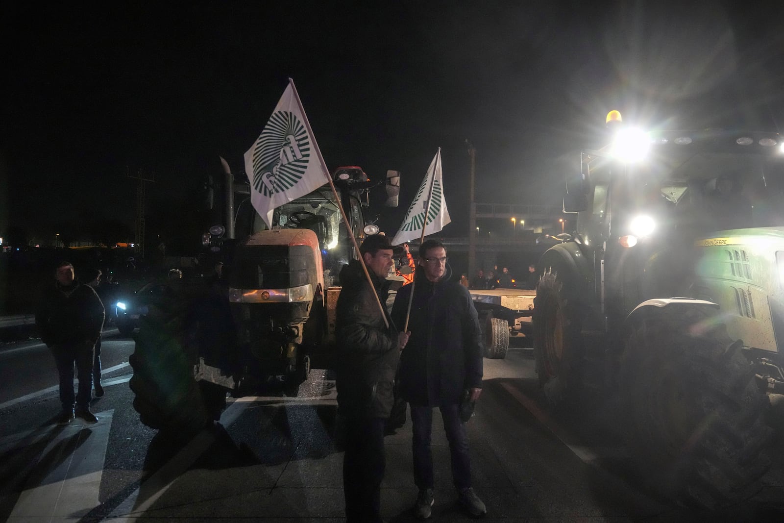 Farmers hold union flags as they stand between tractors on a blocked highway in Velizy-Villacoublay, outside Paris, Sunday, Nov. 17, 2024. (AP Photo/Michel Euler)