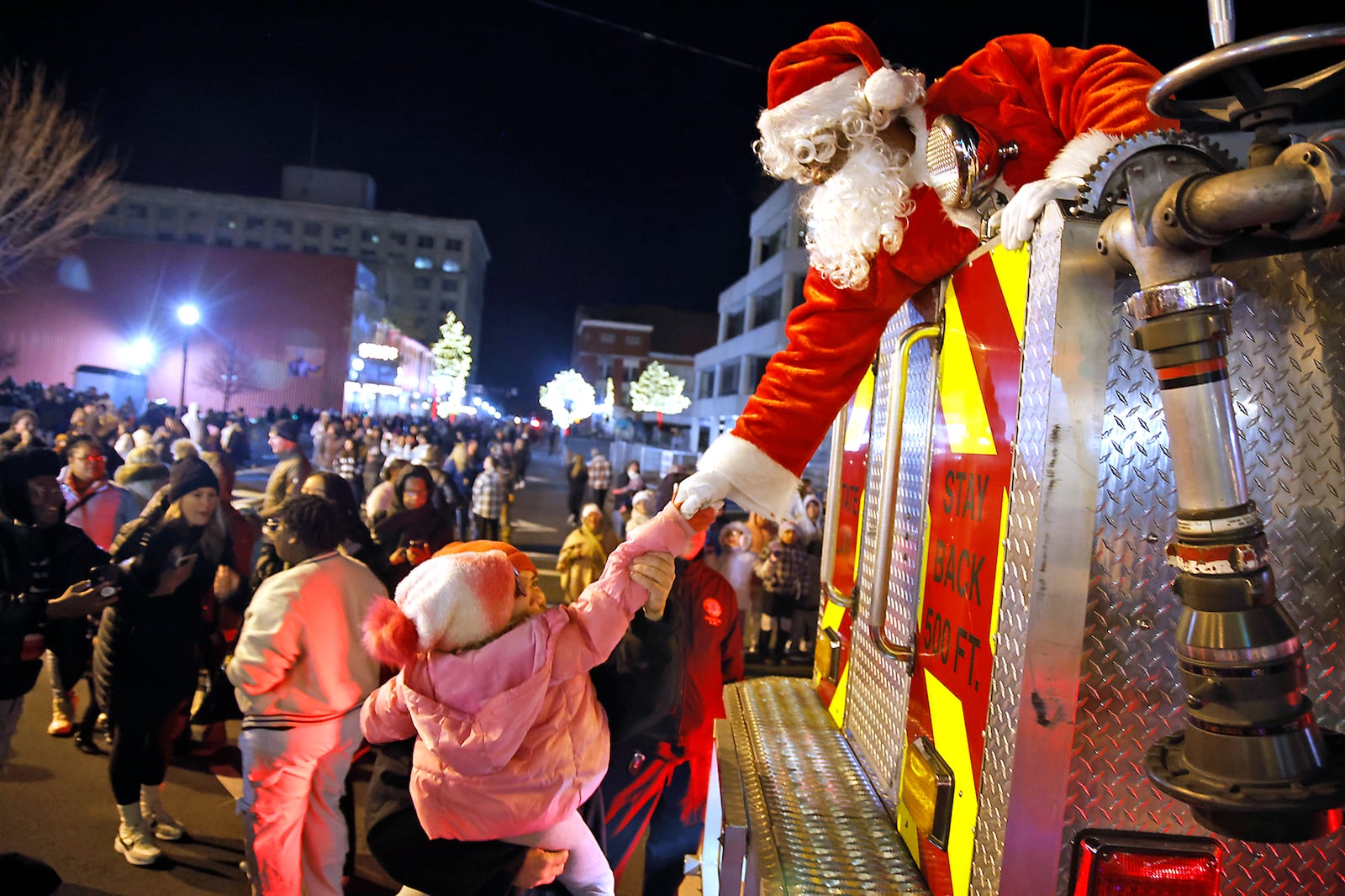 Santa reaches down from the Springfield Fire Division aerial truck to shake a young girls hand Friday, Nov. 24, 2023 during the Springfield Holiday in the City Grand Illumination. Santa arrived in the fire truck and was raised up to turn the city's Christmas tree on. The Illumination kicks off a month of holiday activities in downtown Springfield. BILL LACKEY/STAFF