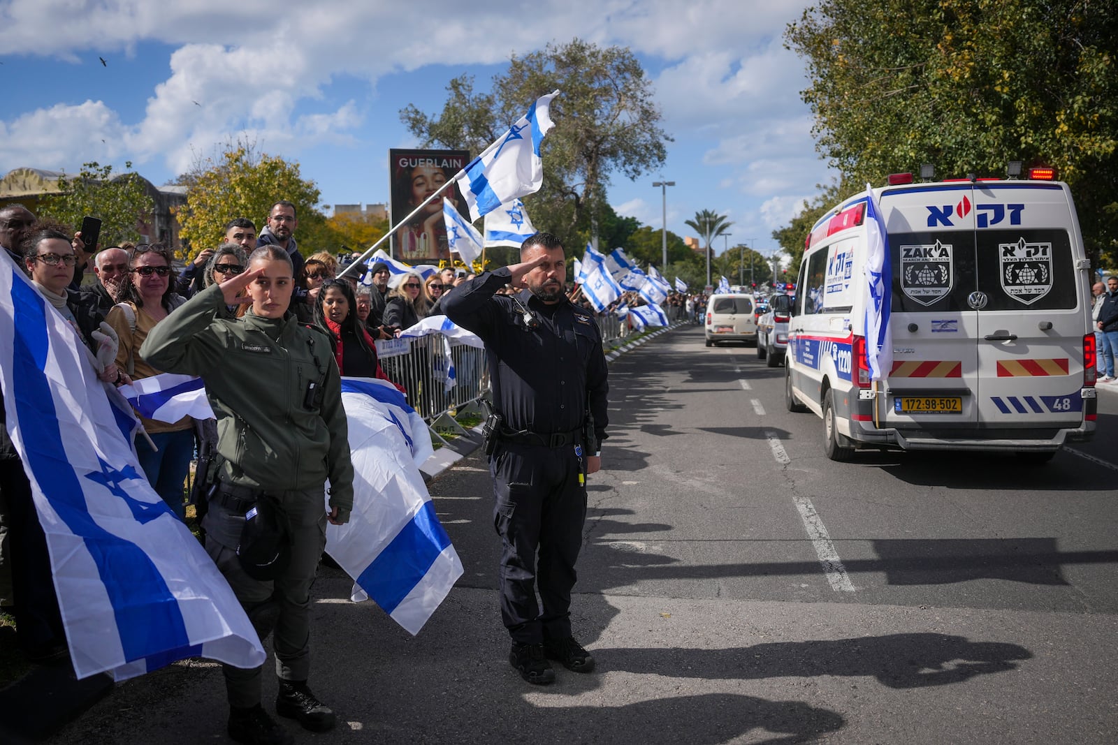 A border policewoman and a policeman salute as a convoy carrying the coffins of four Israeli hostages, including a mother and her two children, arrives at the Abu Kabir Forensic Institute in Tel Aviv, Israel, Thursday Feb. 20, 2025. The bodies were handed over by Palestinian militant groups in Gaza.(AP Photo/Ohad Zwigenberg)