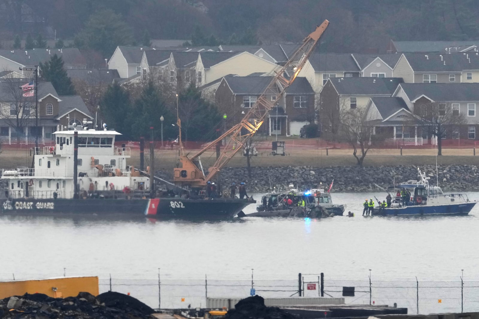 A member of a dive team and a Coast Guard vessel with a crane are pictured as they work near the wreckage of a Black Hawk helicopter in the Potomac River from Ronald Reagan Washington National Airport, Friday, Jan. 31, 2025, in Arlington, Va. (AP Photo/Alex Brandon)