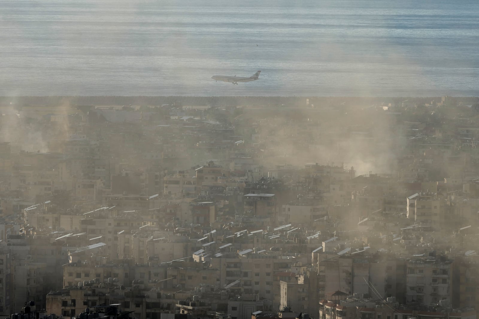 A Middle East Airlines airplane flies over Dahiyeh as smoke rises from Israeli airstrikes in Dahiyeh, Beirut, Lebanon, Tuesday, Nov. 26, 2024. (AP Photo/Bilal Hussein)