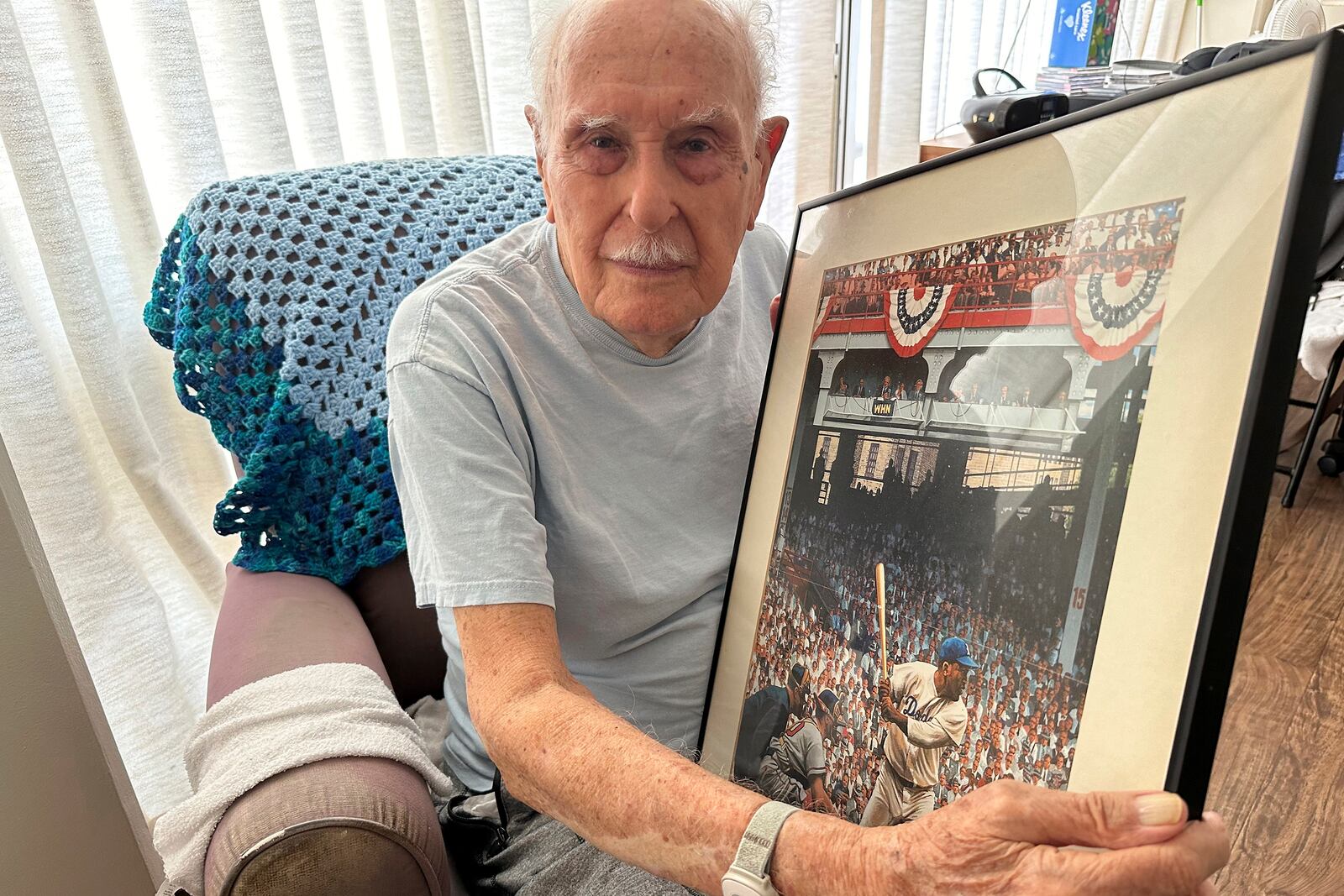 Jim Becker, a former Associated Press journalist, holds a painting depicting Jackie Robinson's Major League Baseball debut in 1947, at his home in Kaneohe, Hawaii, May 21, 2024. (AP Photo/Audrey McAvoy)