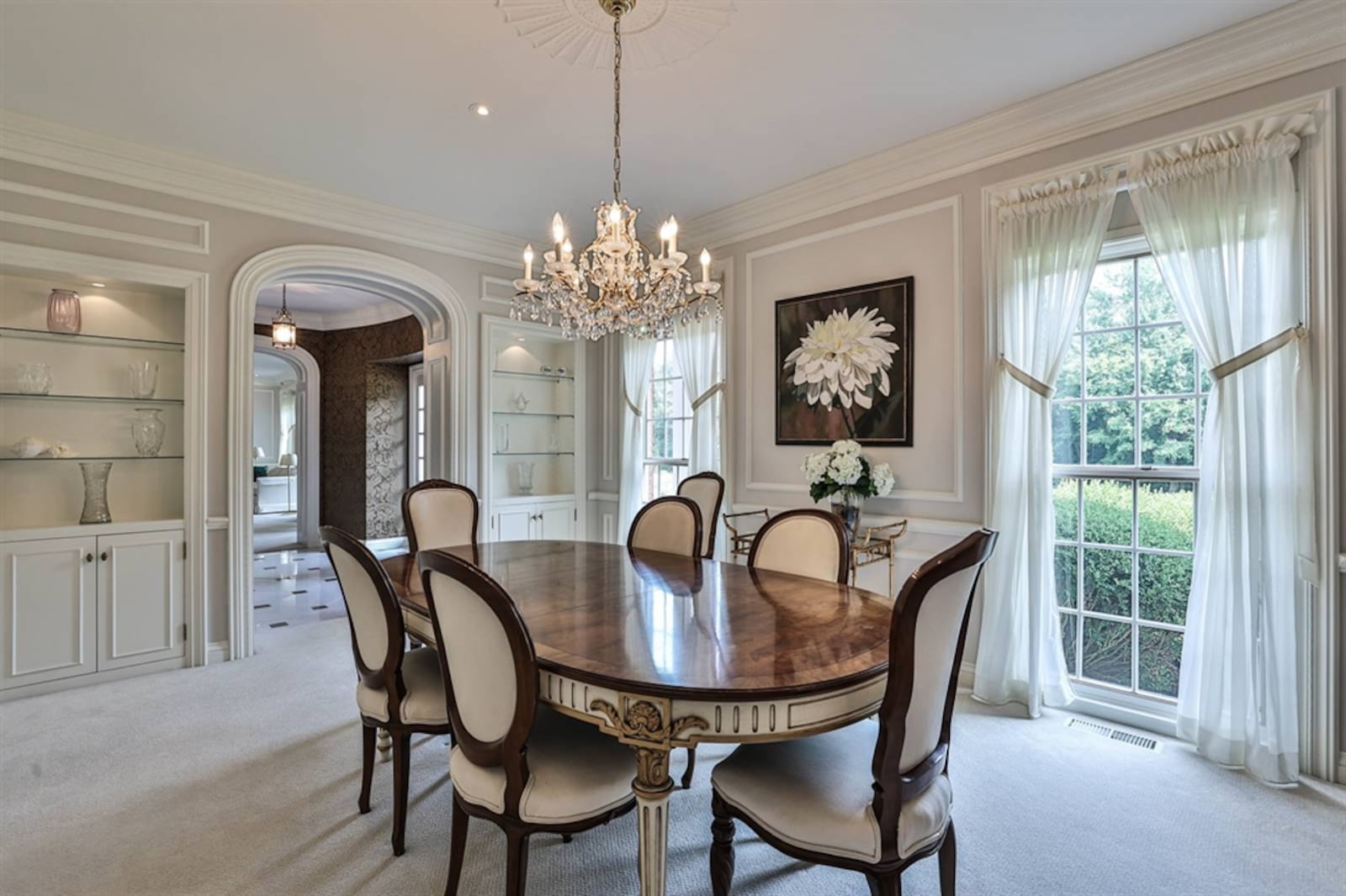 The dining room has floor-to-ceiling windows, a chair rail, wall frames and a crystal chandelier centered within a ceiling medallion. Contributed