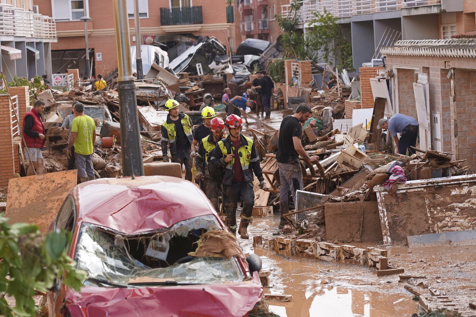 Firefighters walk as people try to clear up the damage after floods in Massanassa, just outside of Valencia, Spain, Friday, Nov. 1, 2024. (AP Photo/Alberto Saiz)