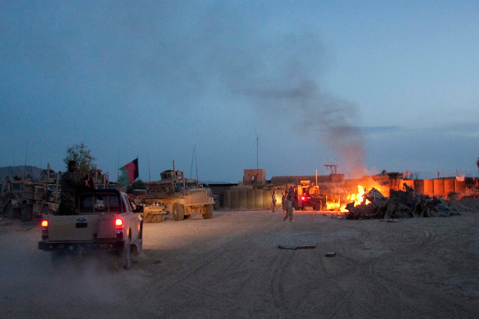 In this April 28, 2011, photo, an Afghan National Army pickup truck passes parked U.S. armored military vehicles, as smoke rises from a fire in a trash burn pit at Forward Operating Base Caferetta Nawzad, Helmand province south of Kabul, Afghanistan. (AP Photo/Simon Klingert, File)