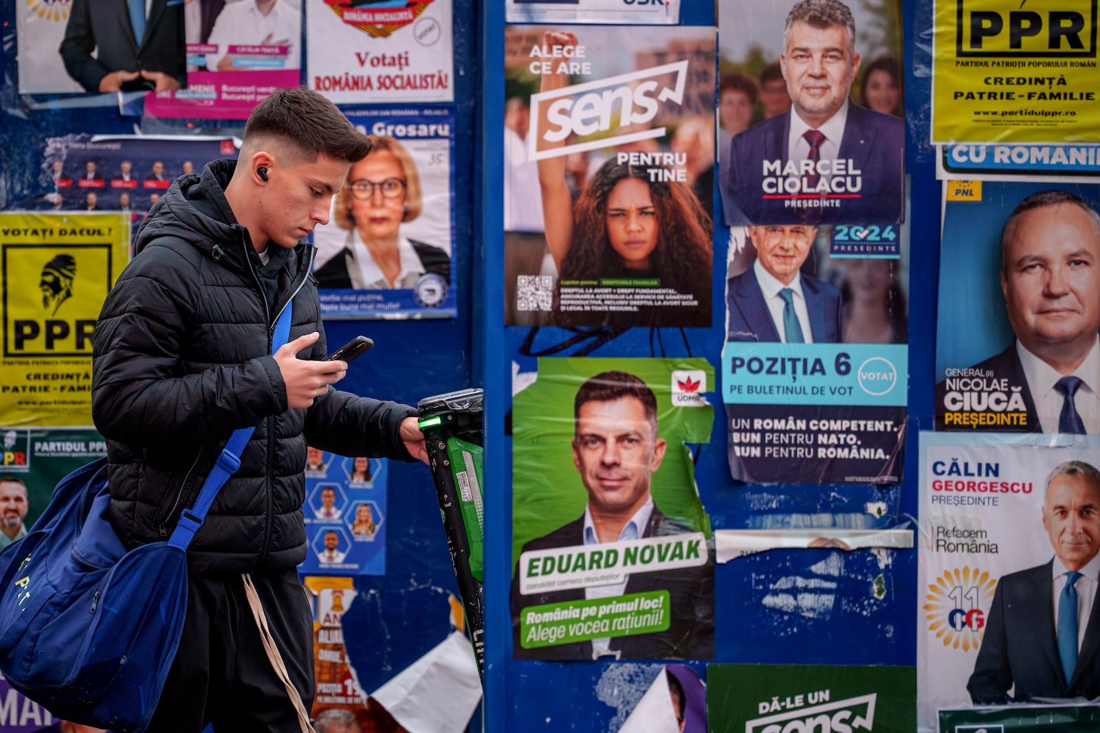 A young man stands by panels displaying electoral posters ahead of the Nov. 24 presidential elections in Bucharest, Romania, Friday, Nov. 22, 2024. (AP Photo/Andreea Alexandru)