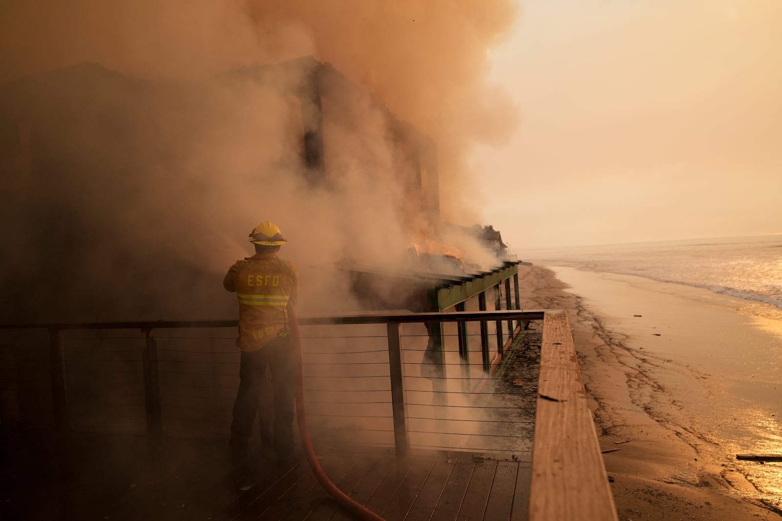 A firefighter protects a beachfront property while fighting the Palisades Fire on Thursday, Jan. 9, 2025, in Malibu, Calif. (AP Photo/Jae C. Hong)