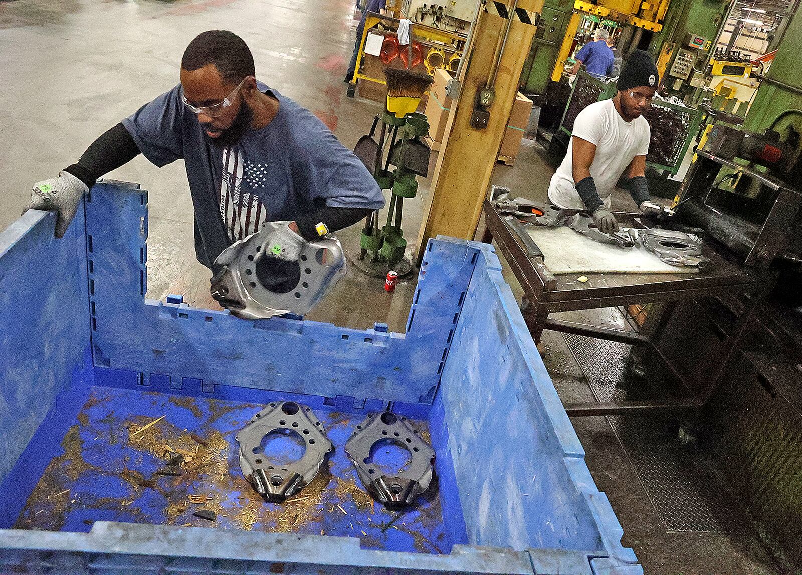 Workers at Pentaflex take parts off a press after they've been stamped Wednesday. BILL LACKEY/STAFF