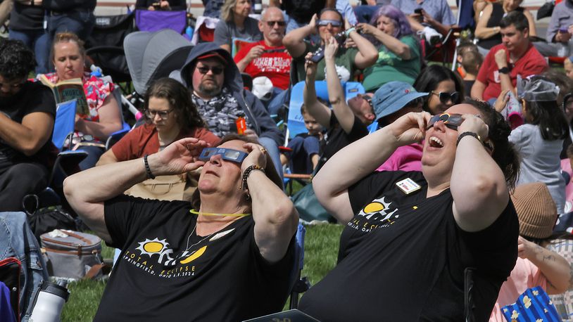 Michelle Hemphill, left, and Teresa Blue-McWhorter watch the solar eclipse start to form over National Road Commons Park Monday, April 8, 2024. BILL LACKEY/STAFF