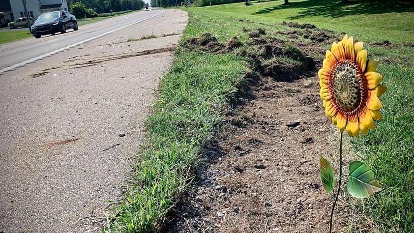 A passerby leaves a sunflower at the scene of a fatal bus crash on Troy Road near Lawrenceville Tuesday August 22, 2023. MARSHALL GORBY \STAFF